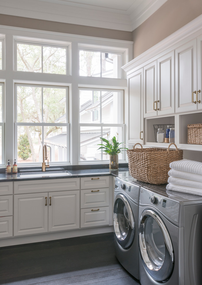 Elegant dark wood floor dedicated laundry room photo with an undermount sink, raised-panel cabinets, white cabinets, beige walls, granite countertops and a side-by-side washer/dryer