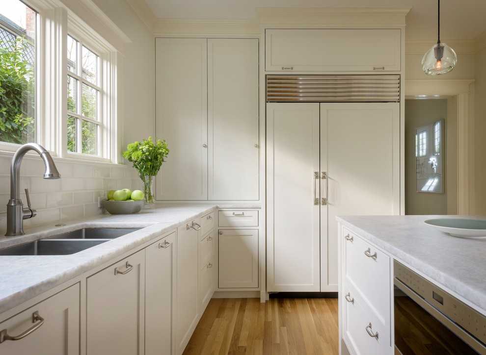 Kitchen - mid-sized transitional light wood floor kitchen idea in Seattle with an undermount sink, shaker cabinets, white cabinets, quartzite countertops, green backsplash, ceramic backsplash, paneled appliances and an island