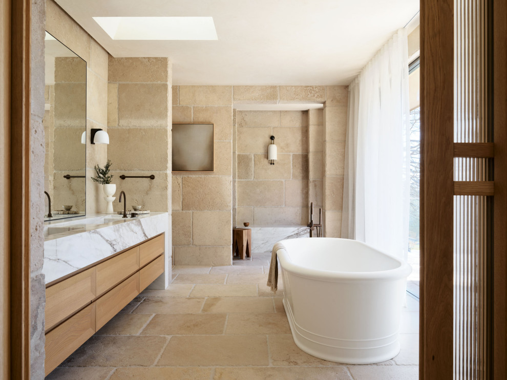 Photo of an expansive transitional master bathroom in Sydney with a freestanding tub, an open shower, stone tile, limestone floors, a double vanity, a built-in vanity, flat-panel cabinets, medium wood cabinets, beige tile, an integrated sink, beige floor and white benchtops.