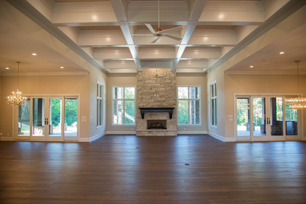 Photo of an expansive open plan living room in Indianapolis with a home bar, beige walls, laminate floors, a standard fireplace, a stone fireplace surround, a wall mounted tv, brown floors and a coffered ceiling.