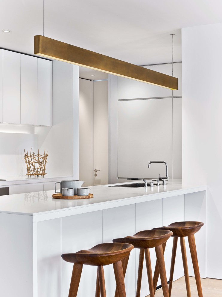 Modern u-shaped kitchen in New York with an undermount sink, flat-panel cabinets, white cabinets, light hardwood floors, with island, beige floor and white benchtop.