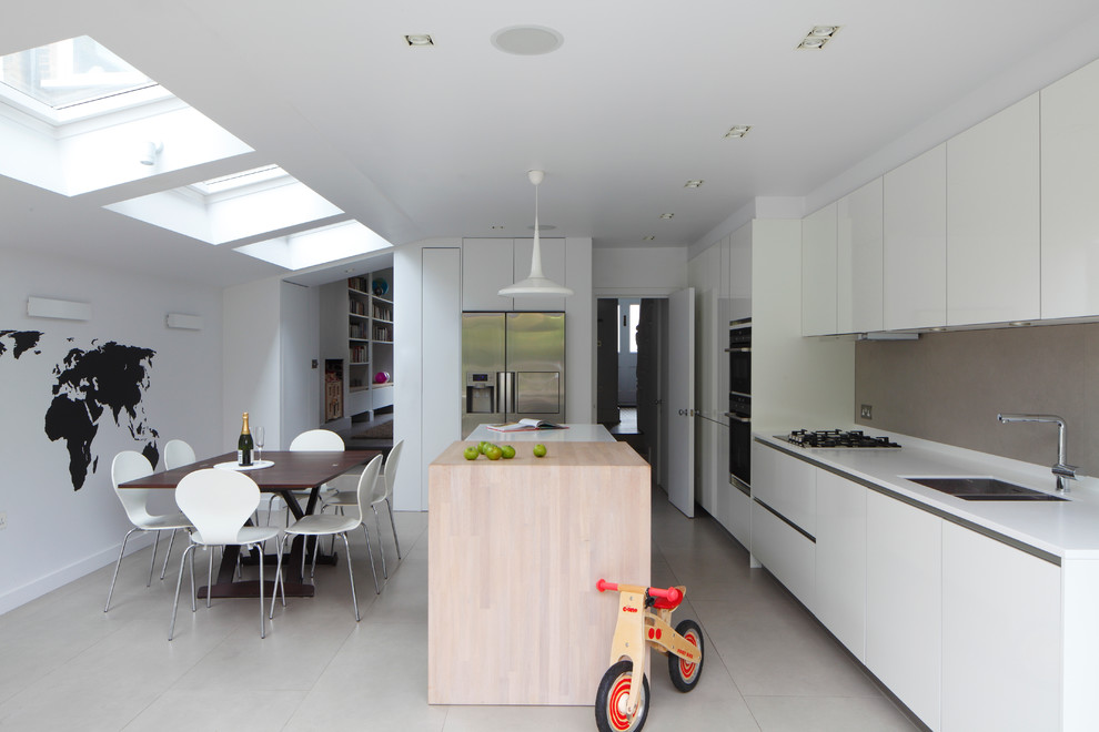 Mid-sized contemporary single-wall open plan kitchen in London with flat-panel cabinets, white cabinets, with island, an integrated sink, solid surface benchtops, grey splashback, ceramic splashback, panelled appliances, ceramic floors, grey floor, white benchtop and vaulted.