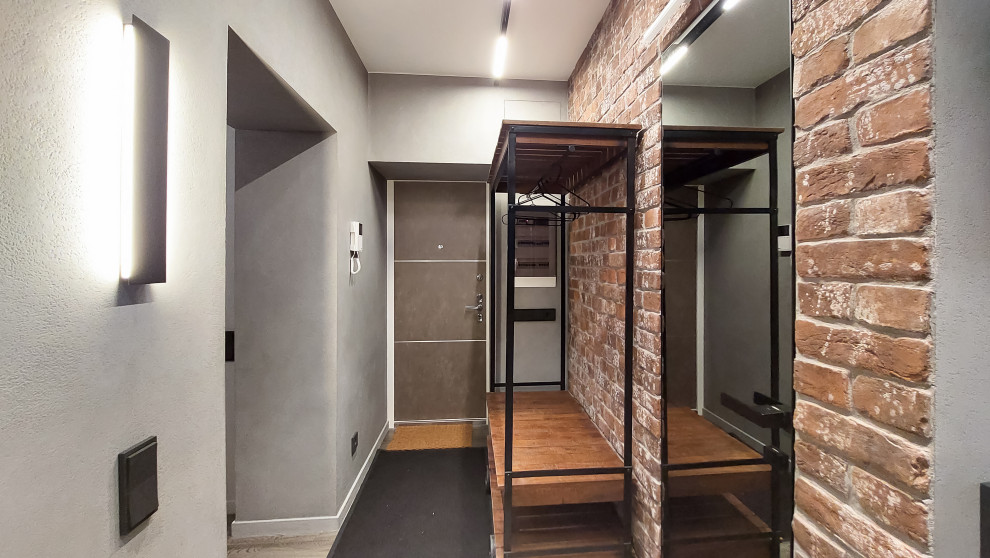 This is an example of a large industrial entry hall in Moscow with grey walls, medium hardwood floors, a single front door, a gray front door, brown floor and brick walls.