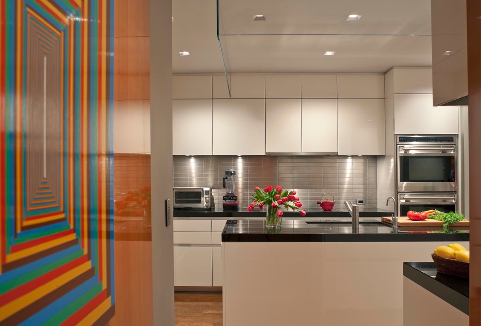 Design ideas for a mid-sized contemporary u-shaped separate kitchen in New York with flat-panel cabinets, metallic splashback, metal splashback, an undermount sink, granite benchtops, stainless steel appliances, medium hardwood floors, with island and black benchtop.
