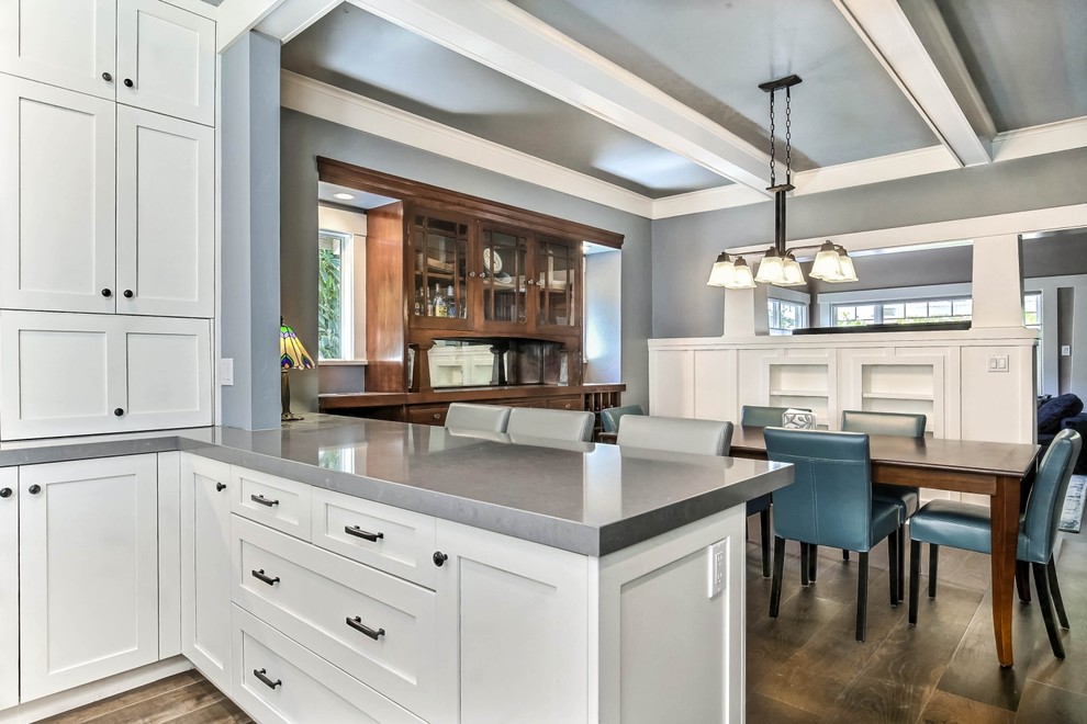 Mid-sized transitional u-shaped eat-in kitchen in San Francisco with a farmhouse sink, shaker cabinets, white cabinets, quartzite benchtops, blue splashback, porcelain splashback, stainless steel appliances, medium hardwood floors, with island, brown floor and grey benchtop.