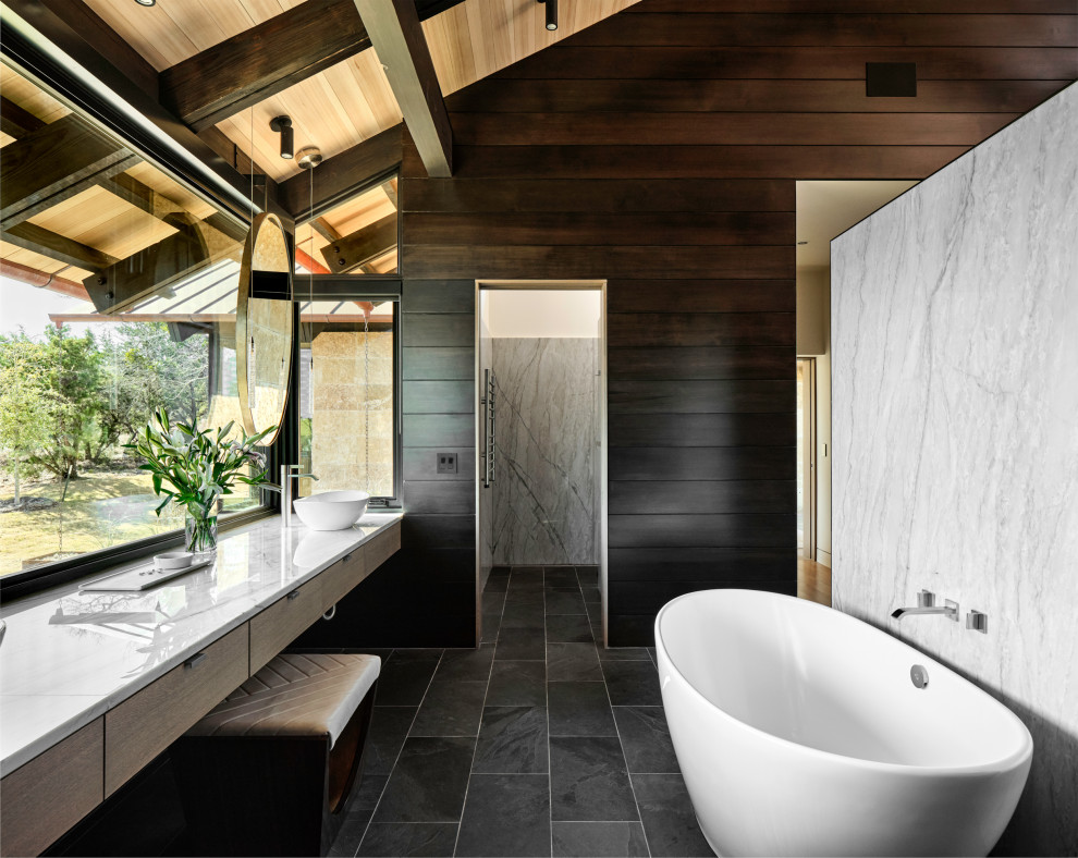 Mid-sized contemporary master bathroom in Austin with flat-panel cabinets, light wood cabinets, a freestanding tub, gray tile, marble, brown walls, slate floors, a vessel sink, quartzite benchtops, black floor, white benchtops, a double vanity, a floating vanity, wood, exposed beam, vaulted and wood walls.