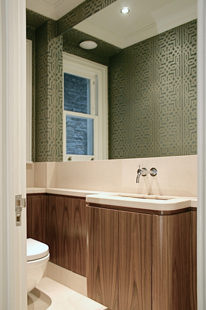 Small transitional powder room in London with flat-panel cabinets, dark wood cabinets, a wall-mount toilet, beige tile, stone slab, green walls, limestone floors, an integrated sink, limestone benchtops, beige floor and beige benchtops.