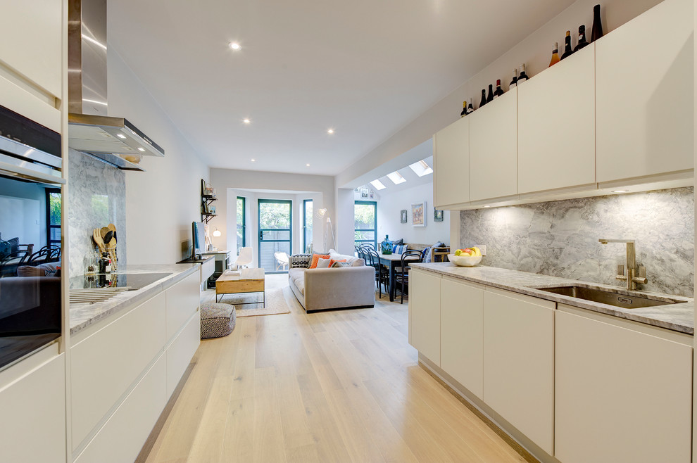 This is an example of a mid-sized contemporary galley eat-in kitchen in London with a drop-in sink, flat-panel cabinets, white cabinets, marble benchtops, grey splashback, marble splashback, panelled appliances, light hardwood floors, no island and grey floor.