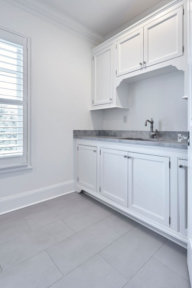 Photo of a mid-sized traditional l-shaped dedicated laundry room in New York with an undermount sink, recessed-panel cabinets, white cabinets, quartzite benchtops, grey walls, porcelain floors and grey floor.