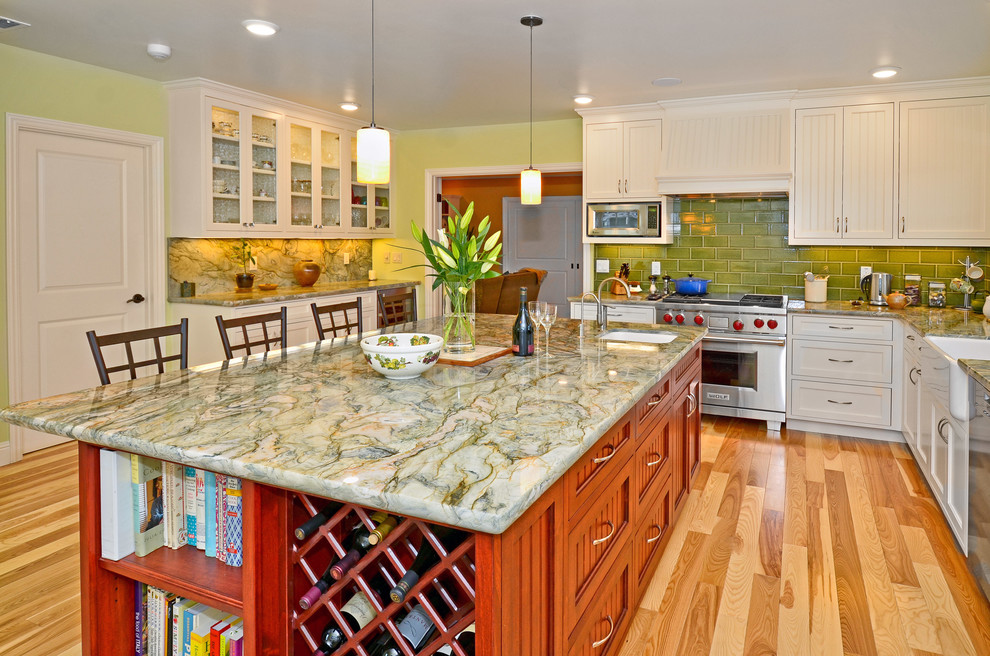 Photo of a large beach style eat-in kitchen in Other with a farmhouse sink, beaded inset cabinets, white cabinets, granite benchtops, green splashback, ceramic splashback, stainless steel appliances, light hardwood floors and with island.