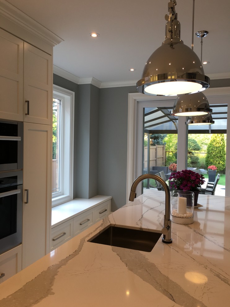 Inspiration for a large transitional l-shaped separate kitchen in Toronto with an undermount sink, shaker cabinets, white cabinets, quartz benchtops, white splashback, stone slab splashback, stainless steel appliances, porcelain floors, with island, white floor and white benchtop.