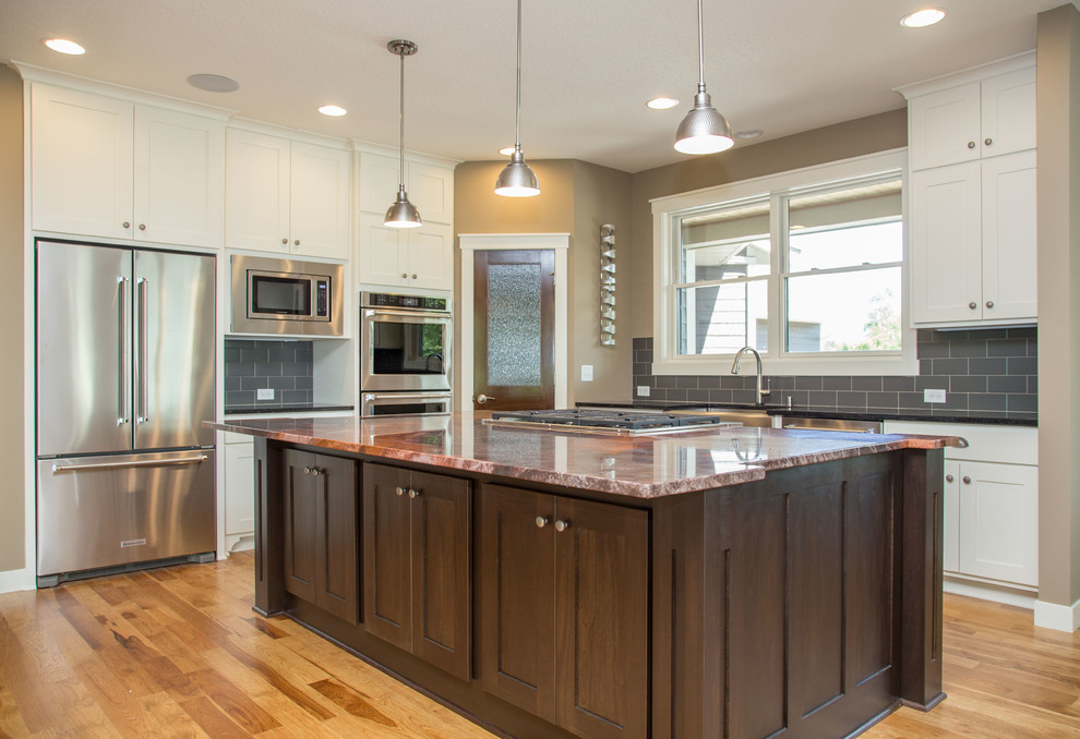 Transitional l-shaped light wood floor eat-in kitchen photo in Minneapolis with a farmhouse sink, shaker cabinets, white cabinets, granite countertops, gray backsplash, ceramic backsplash, stainless steel appliances and an island