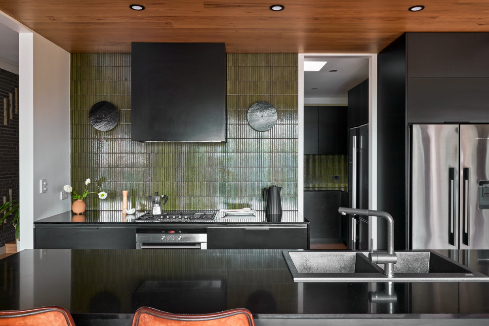 Design ideas for a mid-sized contemporary kitchen in Melbourne with a double-bowl sink, flat-panel cabinets, black cabinets, solid surface benchtops, green splashback, mosaic tile splashback, stainless steel appliances, with island and black benchtop.