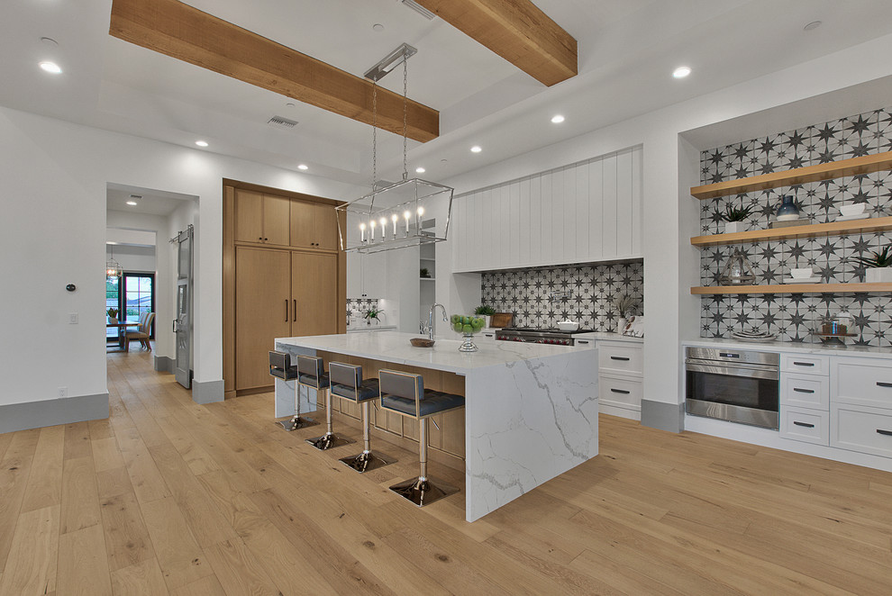 Design ideas for a country l-shaped open plan kitchen in Phoenix with a farmhouse sink, shaker cabinets, white cabinets, stainless steel appliances, medium hardwood floors, with island, brown floor and white benchtop.