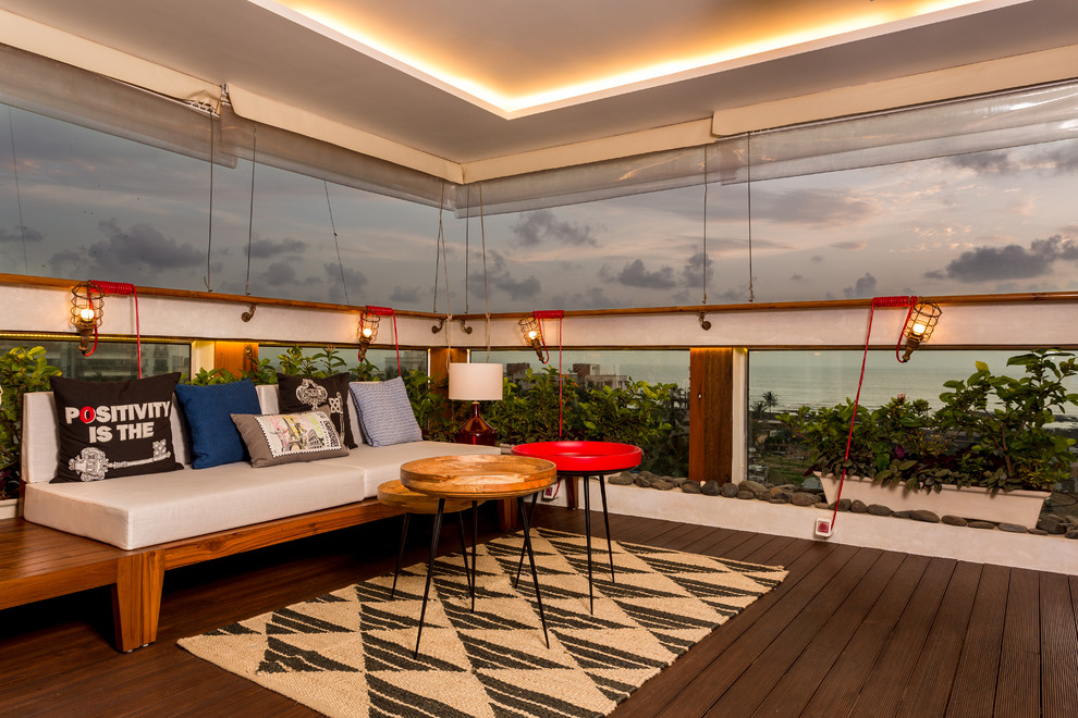 Mid-sized eclectic deck in Mumbai with glass railing and a roof extension.