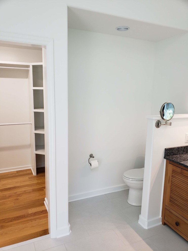 Photo of a large contemporary master bathroom in Raleigh with furniture-like cabinets, medium wood cabinets, a freestanding tub, a corner shower, a two-piece toilet, gray tile, white tile, marble, white walls, ceramic floors, a vessel sink, granite benchtops, white floor, a hinged shower door and black benchtops.