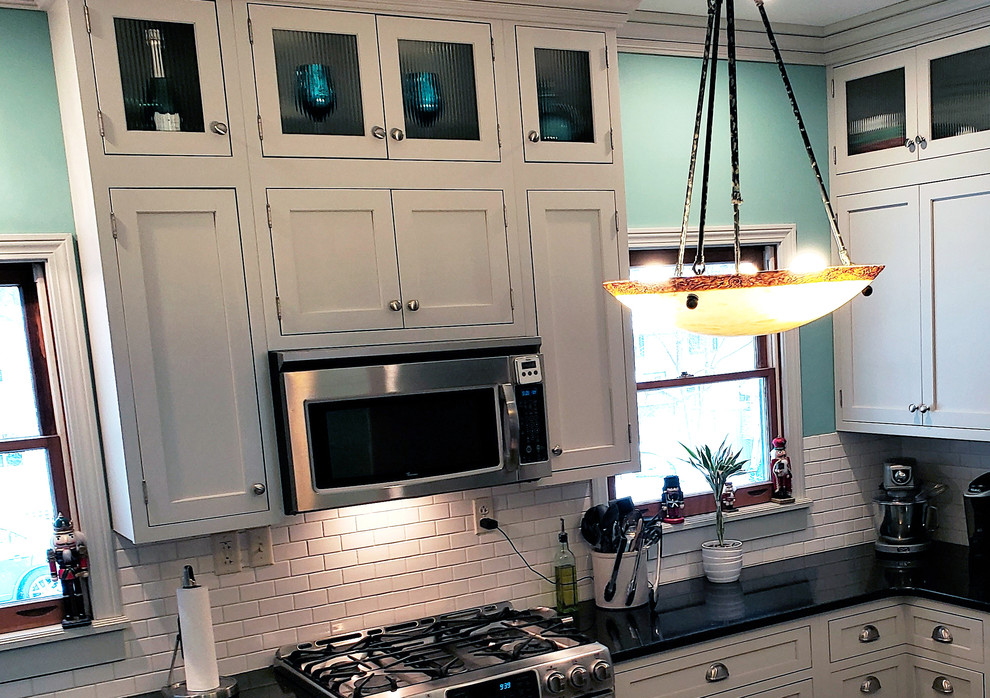 Example of a large transitional u-shaped ceramic tile and beige floor kitchen pantry design with a farmhouse sink, recessed-panel cabinets, white cabinets, quartz countertops, white backsplash, ceramic backsplash, stainless steel appliances, an island and black countertops