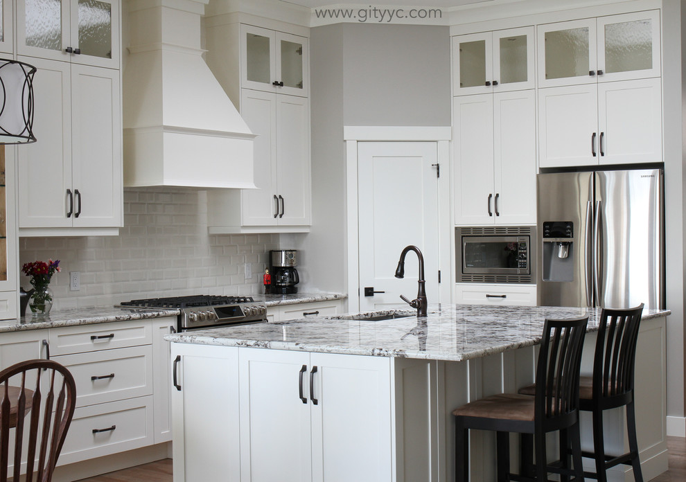 Large transitional l-shaped eat-in kitchen in Calgary with an undermount sink, shaker cabinets, medium wood cabinets, granite benchtops, white splashback, subway tile splashback, stainless steel appliances, medium hardwood floors and with island.