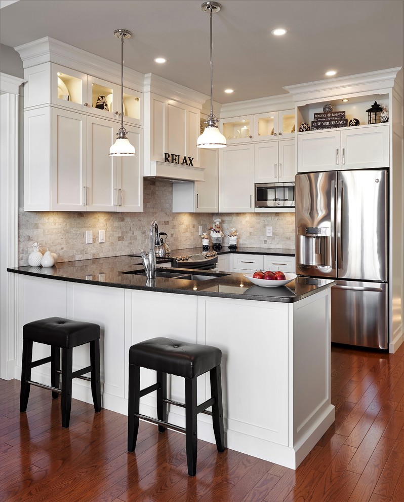 This is an example of a mid-sized transitional u-shaped separate kitchen in Ottawa with shaker cabinets, white cabinets, beige splashback, limestone splashback, stainless steel appliances, a peninsula, black benchtop, a double-bowl sink, medium hardwood floors and brown floor.