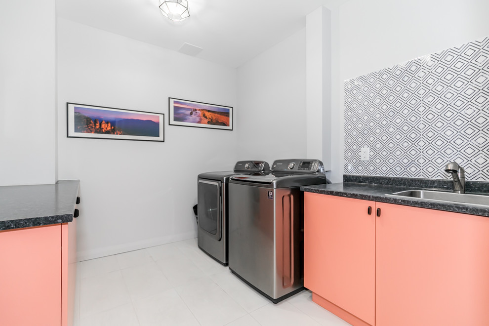 Photo of a mid-sized modern single-wall dedicated laundry room in Other with a drop-in sink, shaker cabinets, orange cabinets, white walls, a side-by-side washer and dryer, white floor and black benchtop.