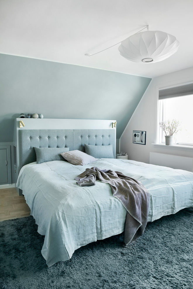 This is an example of a scandinavian bedroom in Copenhagen with blue walls, light hardwood floors and beige floor.