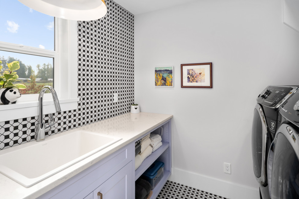 Modelo de cuarto de lavado de galera campestre con fregadero sobremueble, paredes grises, suelo de baldosas de porcelana, lavadora y secadora juntas y encimeras blancas