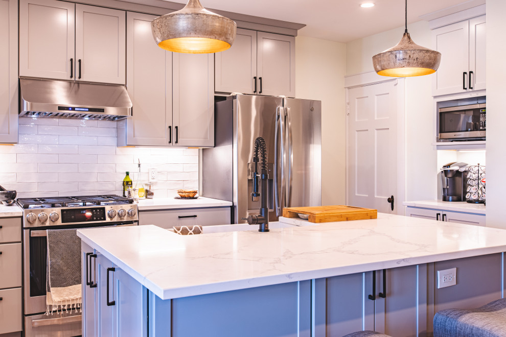 Photo of a mid-sized contemporary l-shaped open plan kitchen in DC Metro with a farmhouse sink, shaker cabinets, grey cabinets, quartzite benchtops, white splashback, subway tile splashback, stainless steel appliances, light hardwood floors, with island, brown floor and white benchtop.