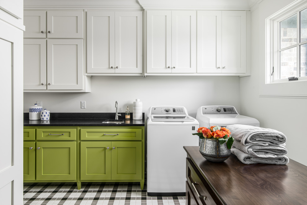 This is an example of a mid-sized transitional dedicated laundry room in Nashville with an undermount sink, shaker cabinets, white walls, porcelain floors, a side-by-side washer and dryer, black benchtop, green cabinets and multi-coloured floor.