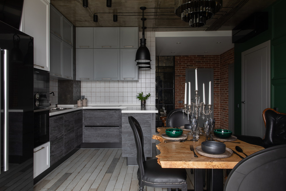 Design ideas for a mid-sized industrial u-shaped open plan kitchen in Other with an undermount sink, flat-panel cabinets, grey cabinets, solid surface benchtops, white splashback, ceramic splashback, black appliances, porcelain floors, a peninsula, grey floor and white benchtop.