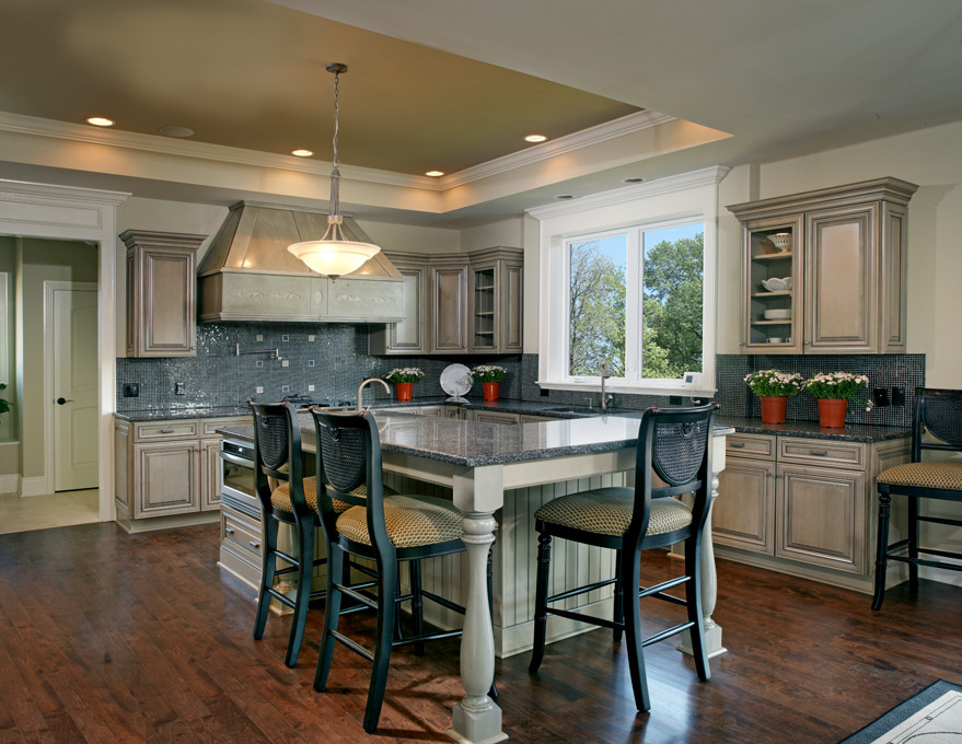 Example of a large transitional l-shaped dark wood floor and brown floor open concept kitchen design in Columbus with a double-bowl sink, stainless steel appliances, mosaic tile backsplash, blue backsplash, raised-panel cabinets, beige cabinets, granite countertops and an island
