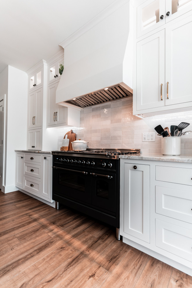 Large transitional l-shaped light wood floor open concept kitchen photo with an undermount sink, shaker cabinets, white cabinets, quartzite countertops, multicolored backsplash, porcelain backsplash, stainless steel appliances and an island