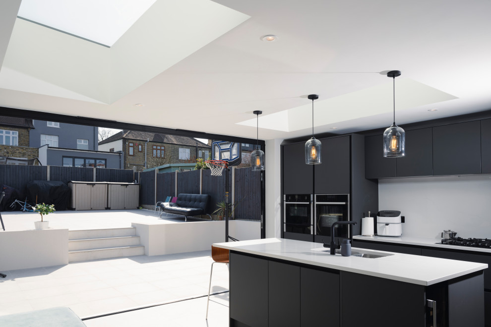На фото: угловая кухня-гостиная в стиле модернизм с черными фасадами, белым фартуком, островом и белой столешницей с