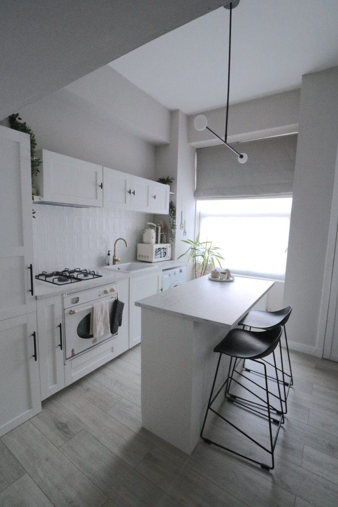 Inspiration för ett litet funkis vit linjärt vitt kök med öppen planlösning, med en undermonterad diskho, skåp i shakerstil, vita skåp, laminatbänkskiva, vitt stänkskydd, stänkskydd i keramik, vita vitvaror, vinylgolv, en köksö och beiget golv