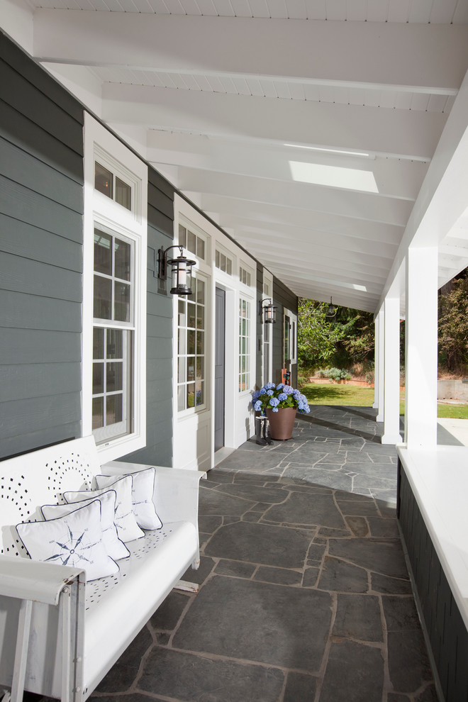 This is an example of a traditional verandah in Vancouver with natural stone pavers and a roof extension.
