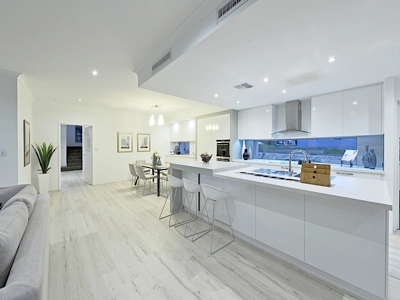 Large modern kitchen in Perth with a double-bowl sink, white cabinets, quartz benchtops, white splashback, glass sheet splashback, light hardwood floors, with island and stainless steel appliances.