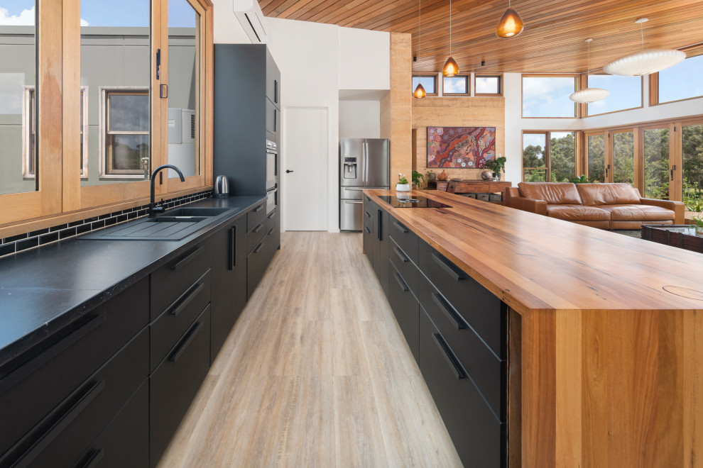 Inspiration for a contemporary galley open plan kitchen in Other with a double-bowl sink, wood worktops, black splashback, ceramic splashback, black appliances, medium hardwood flooring and an island.