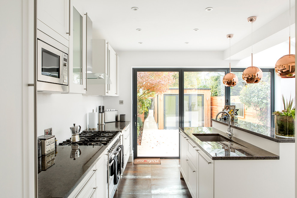 This is an example of a mid-sized contemporary l-shaped open plan kitchen in London with white cabinets, an undermount sink, stainless steel appliances, brown floor, black benchtop, with island, shaker cabinets and granite benchtops.