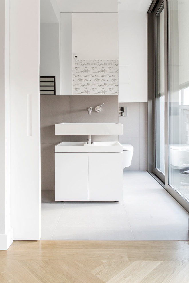 Inspiration for a contemporary bathroom in Berlin with flat-panel cabinets, white cabinets, white walls, a wall-mount sink and brown tile.
