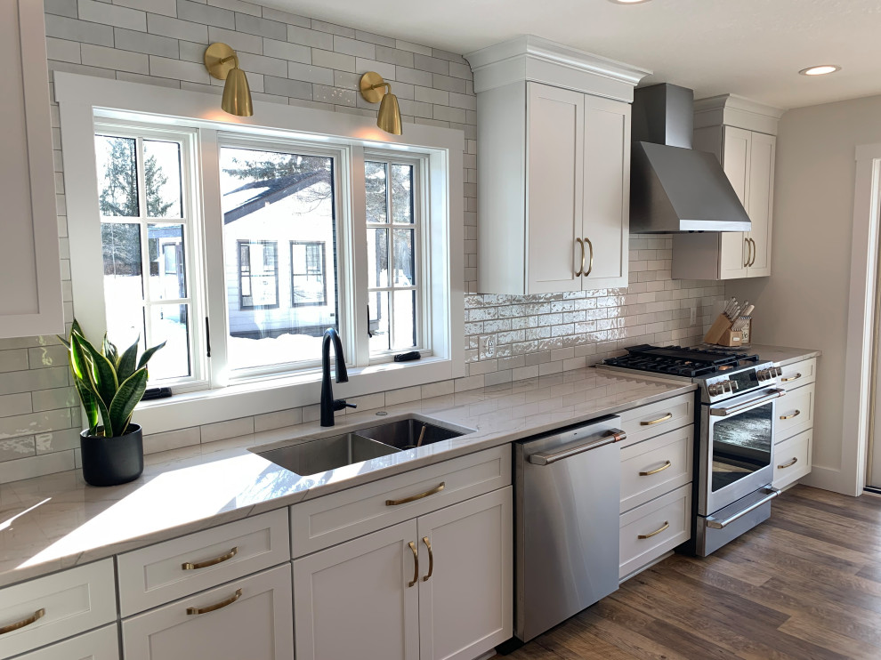 Klassisk inredning av ett stort grå grått kök, med en undermonterad diskho, skåp i shakerstil, vita skåp, bänkskiva i kvarts, rostfria vitvaror, vinylgolv, en köksö och brunt golv