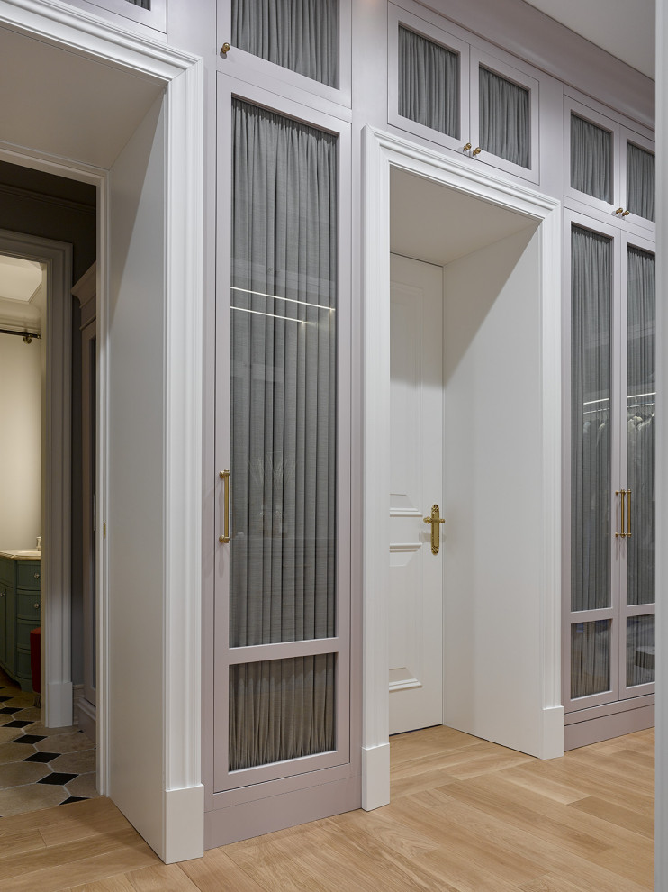 Large contemporary gender-neutral walk-in wardrobe in Moscow with glass-front cabinets, grey cabinets, light hardwood floors and yellow floor.