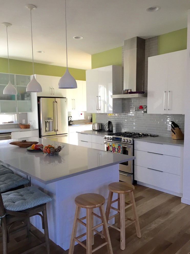 Photo of a scandinavian kitchen in Denver with flat-panel cabinets, white cabinets, subway tile splashback, stainless steel appliances, medium hardwood floors, with island, a farmhouse sink and white splashback.