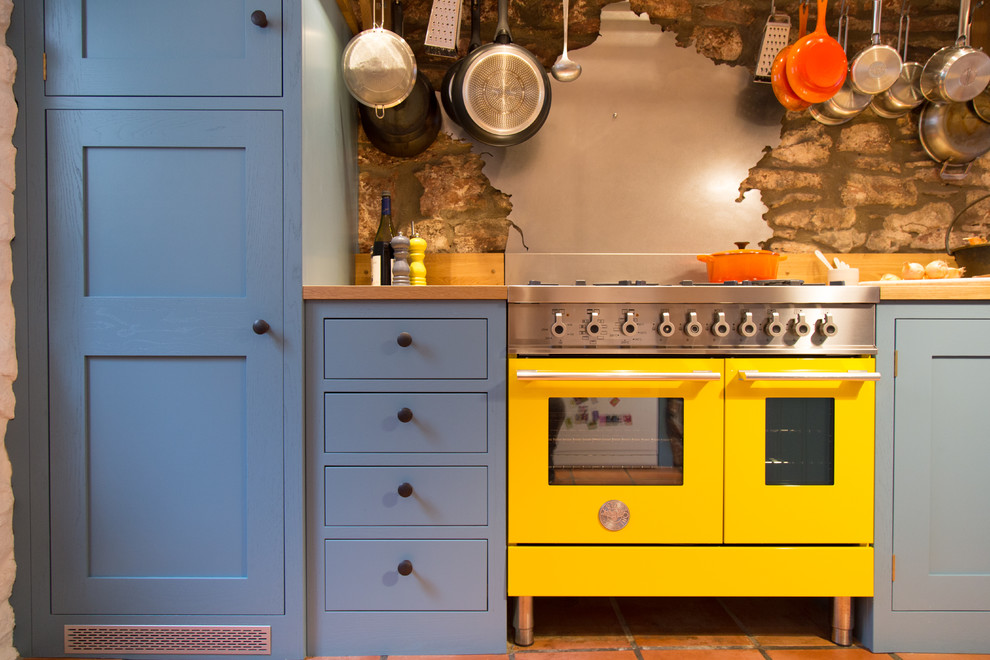 Inspiration for a small contemporary galley separate kitchen in Other with a farmhouse sink, shaker cabinets, blue cabinets, wood benchtops, metallic splashback, metal splashback, coloured appliances, with island and terra-cotta floors.