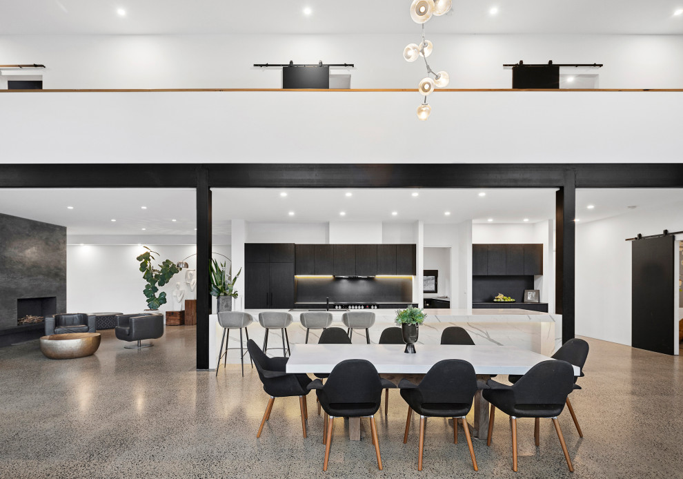 Large modern galley open plan kitchen in Melbourne with a built-in sink, flat-panel cabinets, black cabinets, engineered stone countertops, black splashback, engineered quartz splashback, black appliances, concrete flooring, an island, multicoloured worktops and a vaulted ceiling.