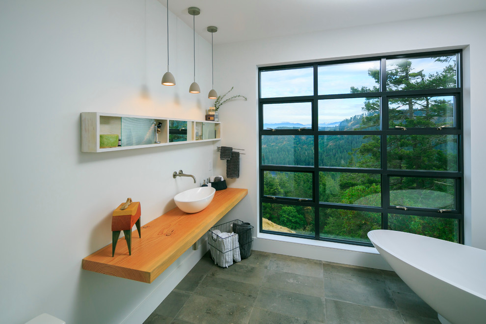 Inspiration for a mid-sized contemporary master bathroom in Vancouver with open cabinets, a freestanding tub, white walls, travertine floors, a vessel sink, wood benchtops, an open shower, gray tile and stone tile.