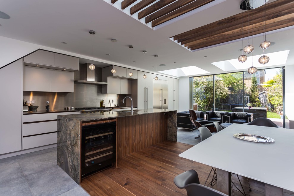 This is an example of a large contemporary single-wall open plan kitchen in London with flat-panel cabinets, grey cabinets, granite benchtops, metallic splashback, stainless steel appliances, with island and multi-coloured benchtop.