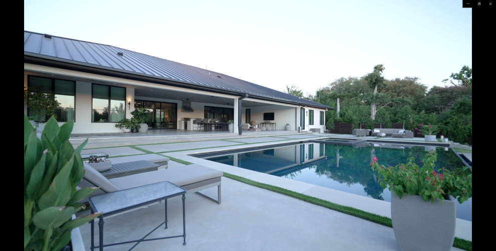 Foto di una grande piscina a sfioro infinito moderna rettangolare dietro casa con una vasca idromassaggio e lastre di cemento