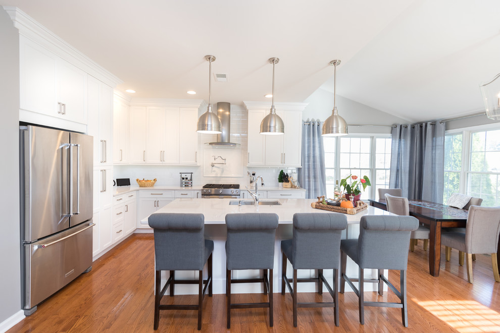 Example of a large transitional l-shaped light wood floor eat-in kitchen design in DC Metro with an undermount sink, shaker cabinets, white cabinets, quartz countertops, white backsplash, subway tile backsplash, stainless steel appliances and an island
