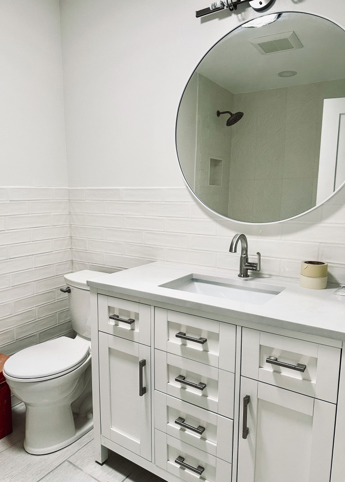 Bild på ett litet funkis grå grått badrum, med skåp i shakerstil, vita skåp, ett badkar i en alkov, en dusch i en alkov, en toalettstol med separat cisternkåpa, vit kakel, keramikplattor, vita väggar, klinkergolv i keramik, ett undermonterad handfat, bänkskiva i kvarts och grått golv
