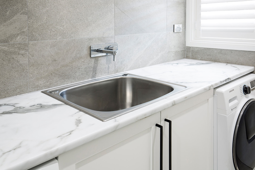 Photo of a large transitional galley dedicated laundry room in Sydney with a single-bowl sink, shaker cabinets, white cabinets, laminate benchtops, multi-coloured walls, porcelain floors, a side-by-side washer and dryer, multi-coloured floor and multi-coloured benchtop.