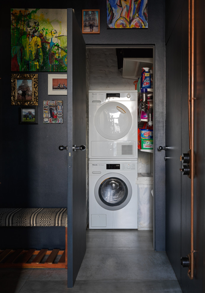 Foto de armario lavadero lineal industrial pequeño con paredes blancas, suelo de baldosas de porcelana, lavadora y secadora apiladas y suelo gris